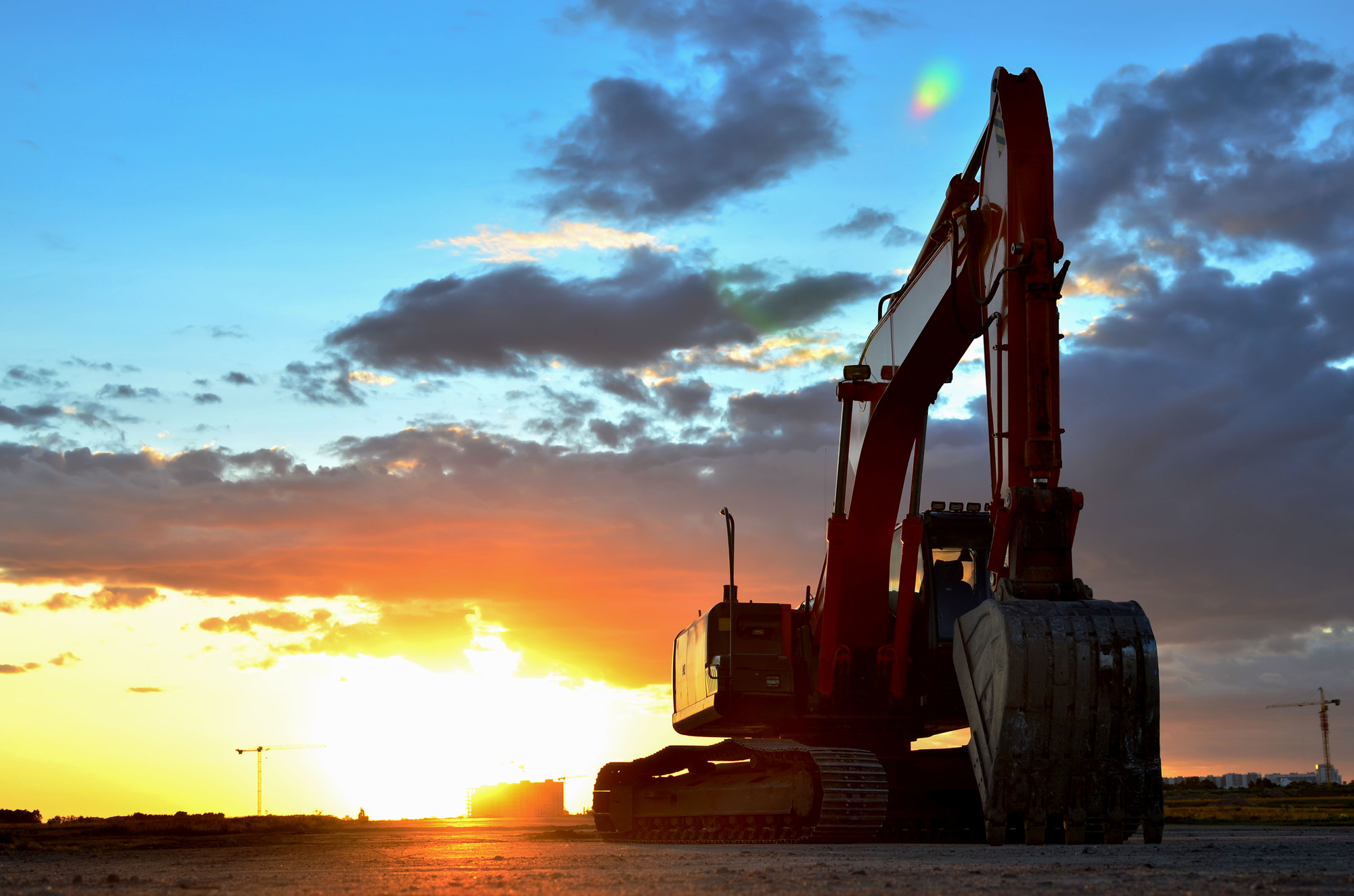 Large tracked excavator on a construction site against the background of the awesome sunset. Road repair, asphalt replacement. Small roughness sharpness, possible granularity - Image